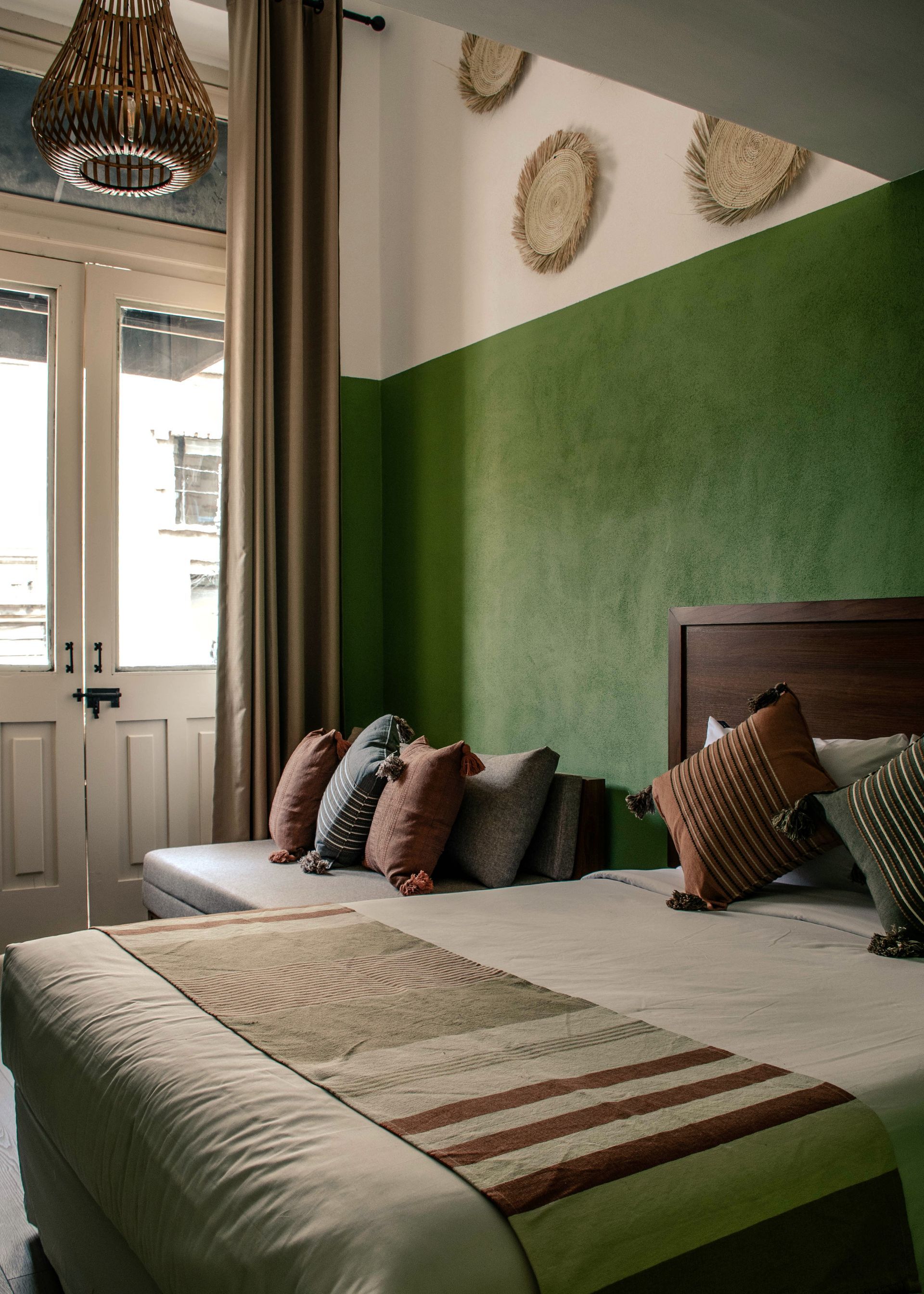 Dormitorio acogedor con paredes verdes y blancas, cama doble, cojines estampados y una puerta acristalada que da al balcón