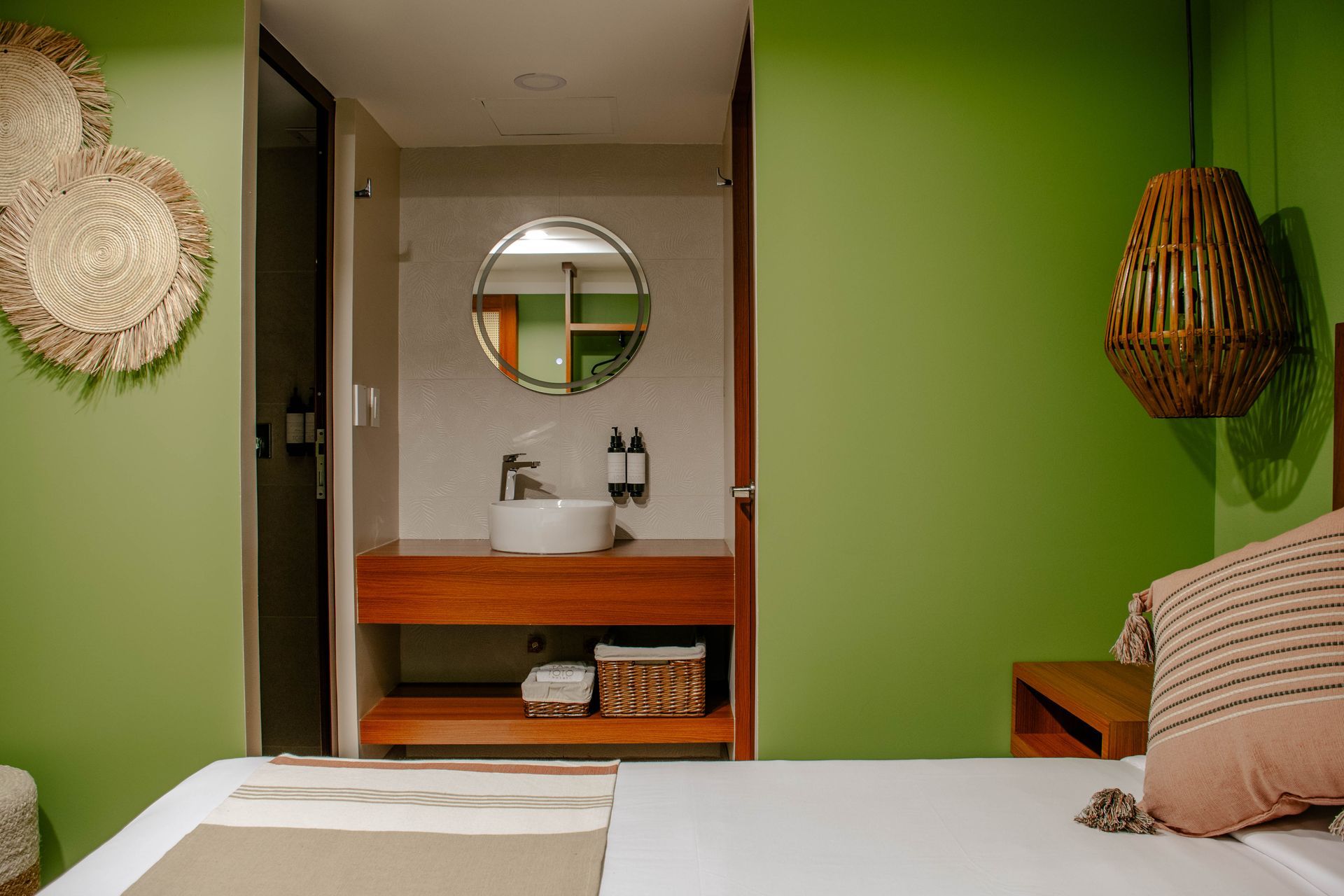 Dormitorio verde con cama blanca, tocador de madera, espejo redondo y decoración de pared tejida