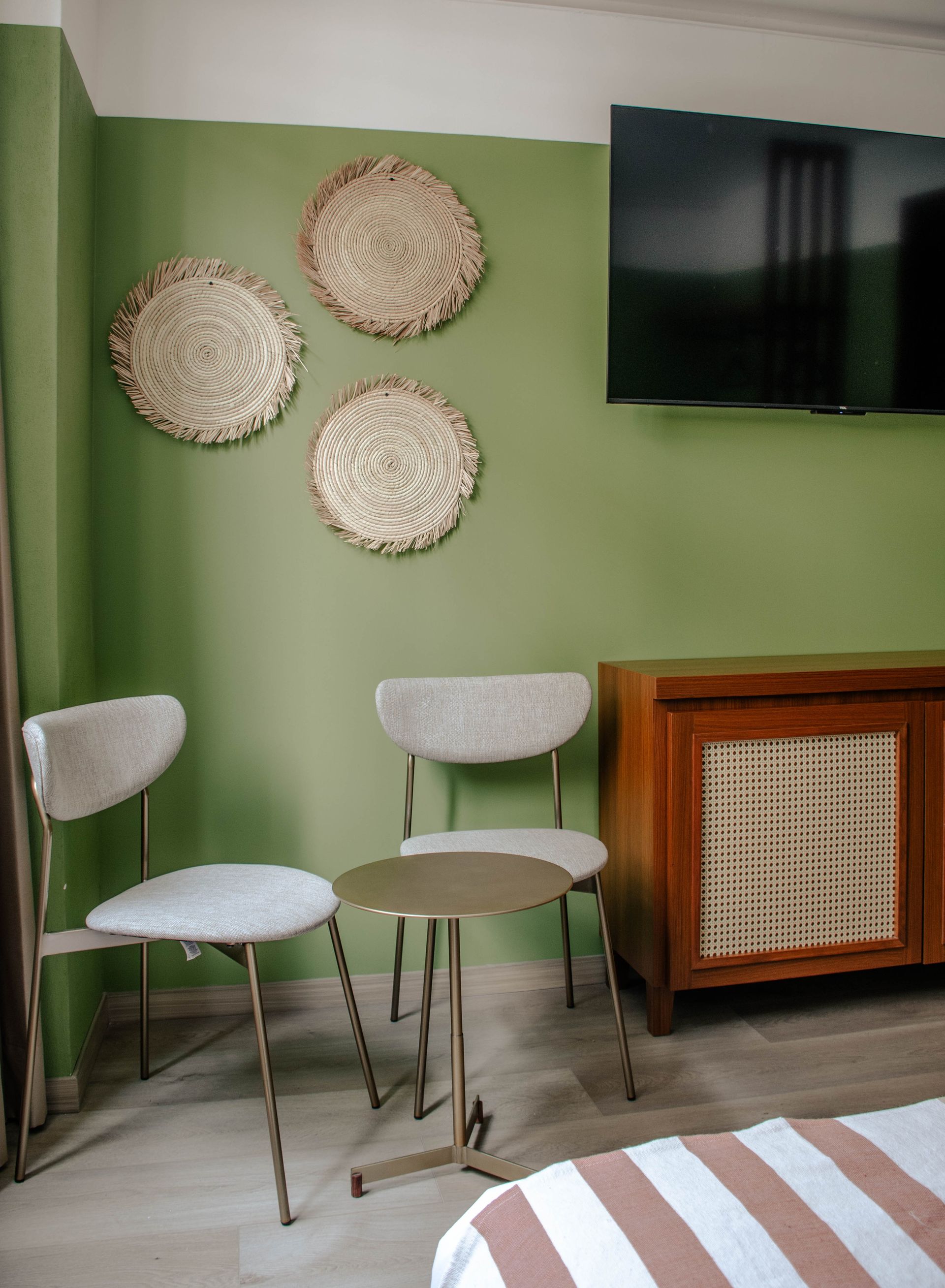 Habitación con paredes verdes, dos sillas blancas, placas decorativas en la pared y un televisor sobre un mueble de madera.