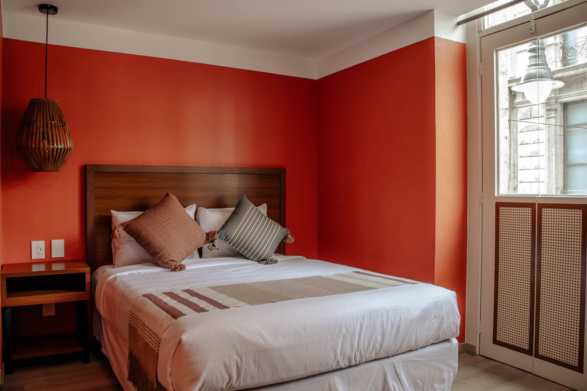 Acogedor dormitorio con paredes rojas, una cama blanca, un cabecero de madera y una ventana con cortinas translúcidas