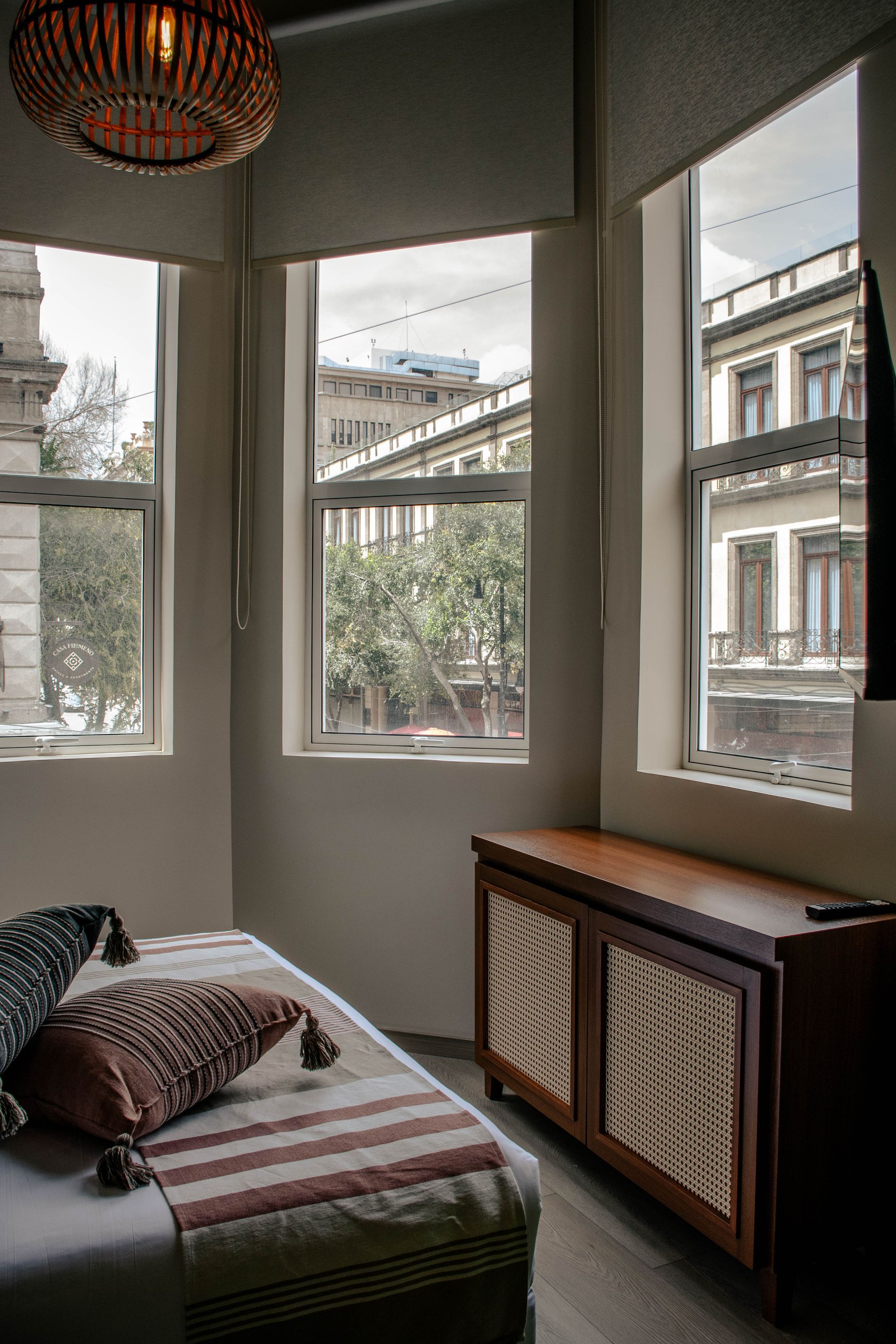 Acogedor rincón junto a la ventana con un diván, una manta a rayas y edificios de la ciudad a la vista.