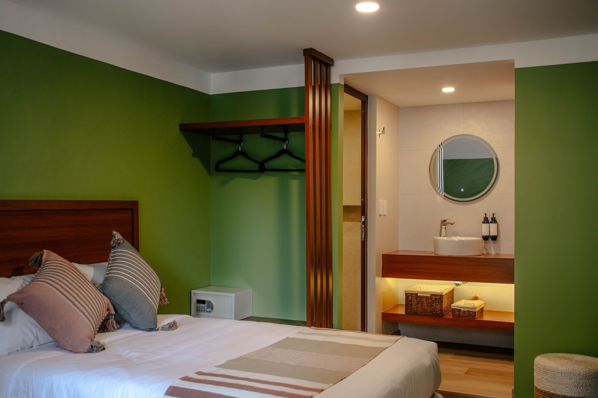 Dormitorio con paredes verdes, cama y tocador con espejo redondo e iluminación cálida
