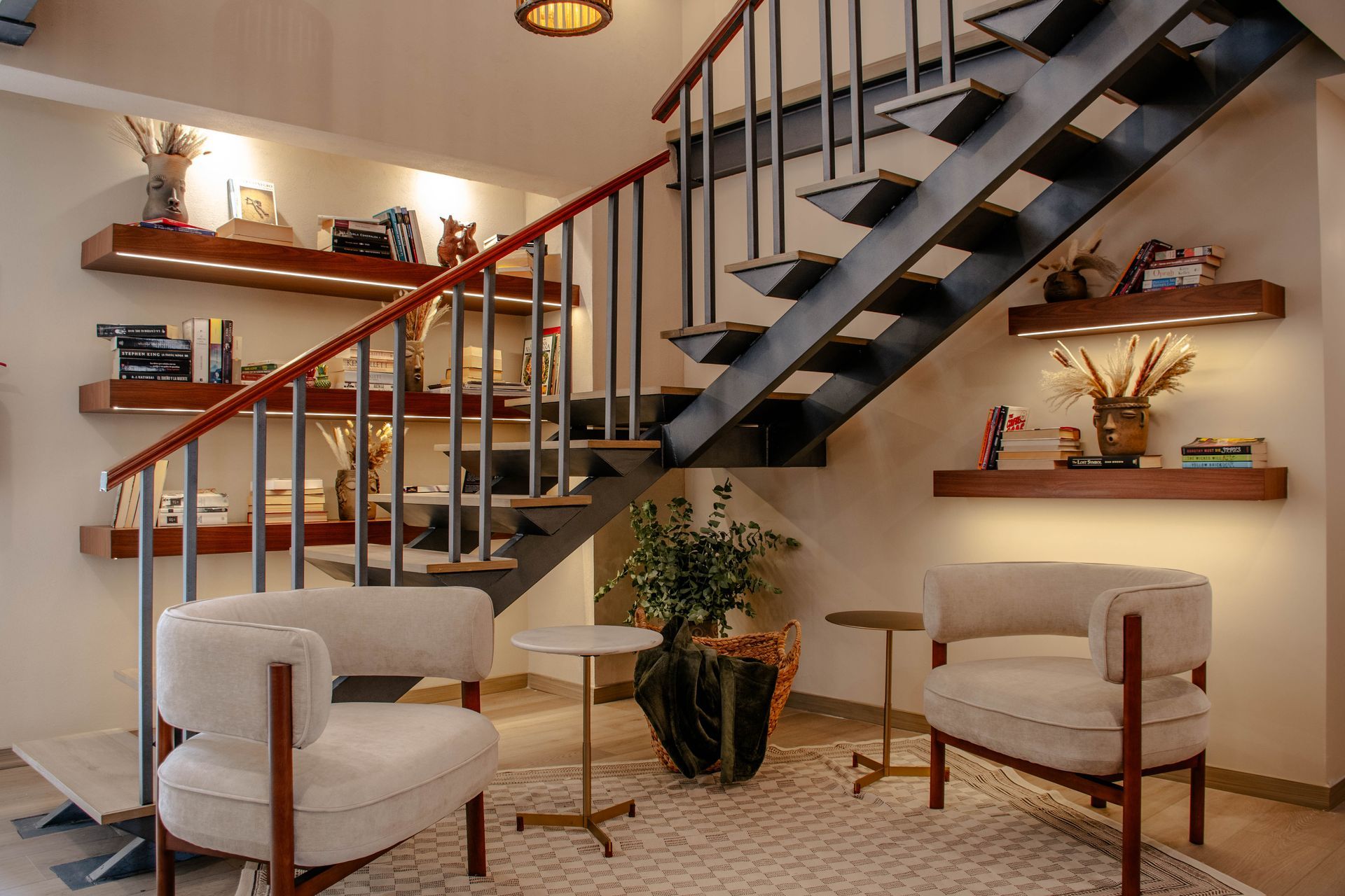 Salón moderno con escaleras, dos sillas blancas, una mesita, estanterías e iluminación cálida