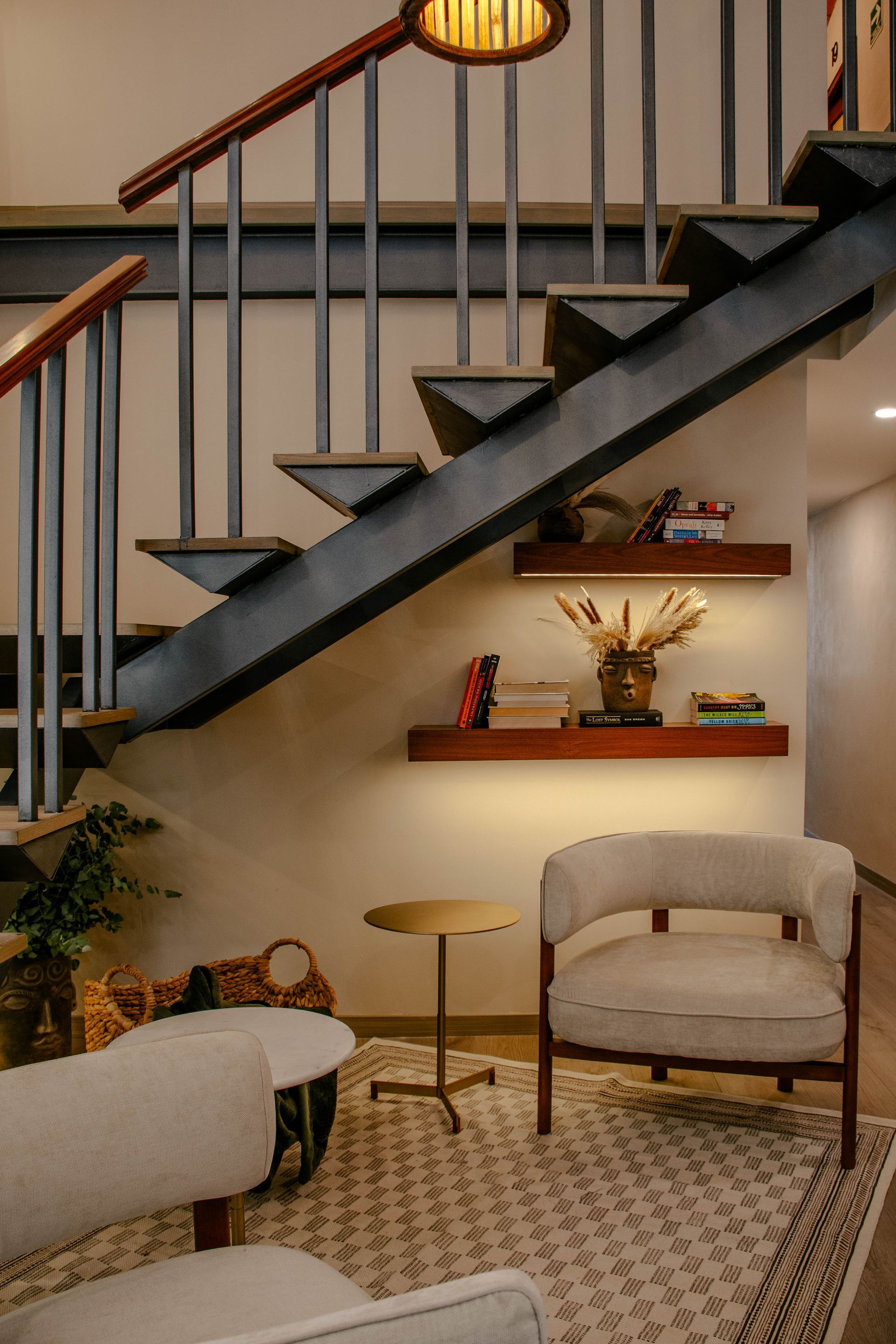 Acogedora sala de estar con escalera, sillón beige, mesa redonda, estanterías e iluminación cálida