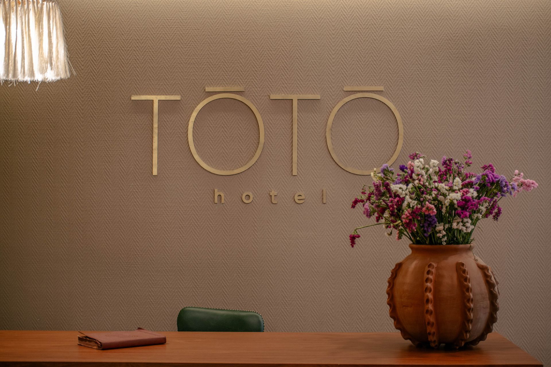 Letrero de TOTO en el vestíbulo de un hotel, sobre un escritorio de madera con un jarrón de flores rosas