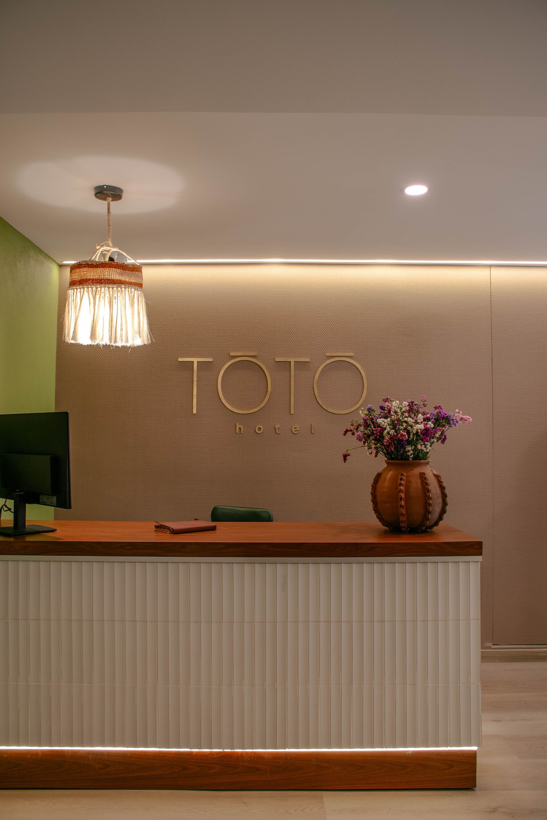 Mostrador minimalista de recepción de hotel con un letrero de TOTO, iluminación cálida y un jarrón con flores
