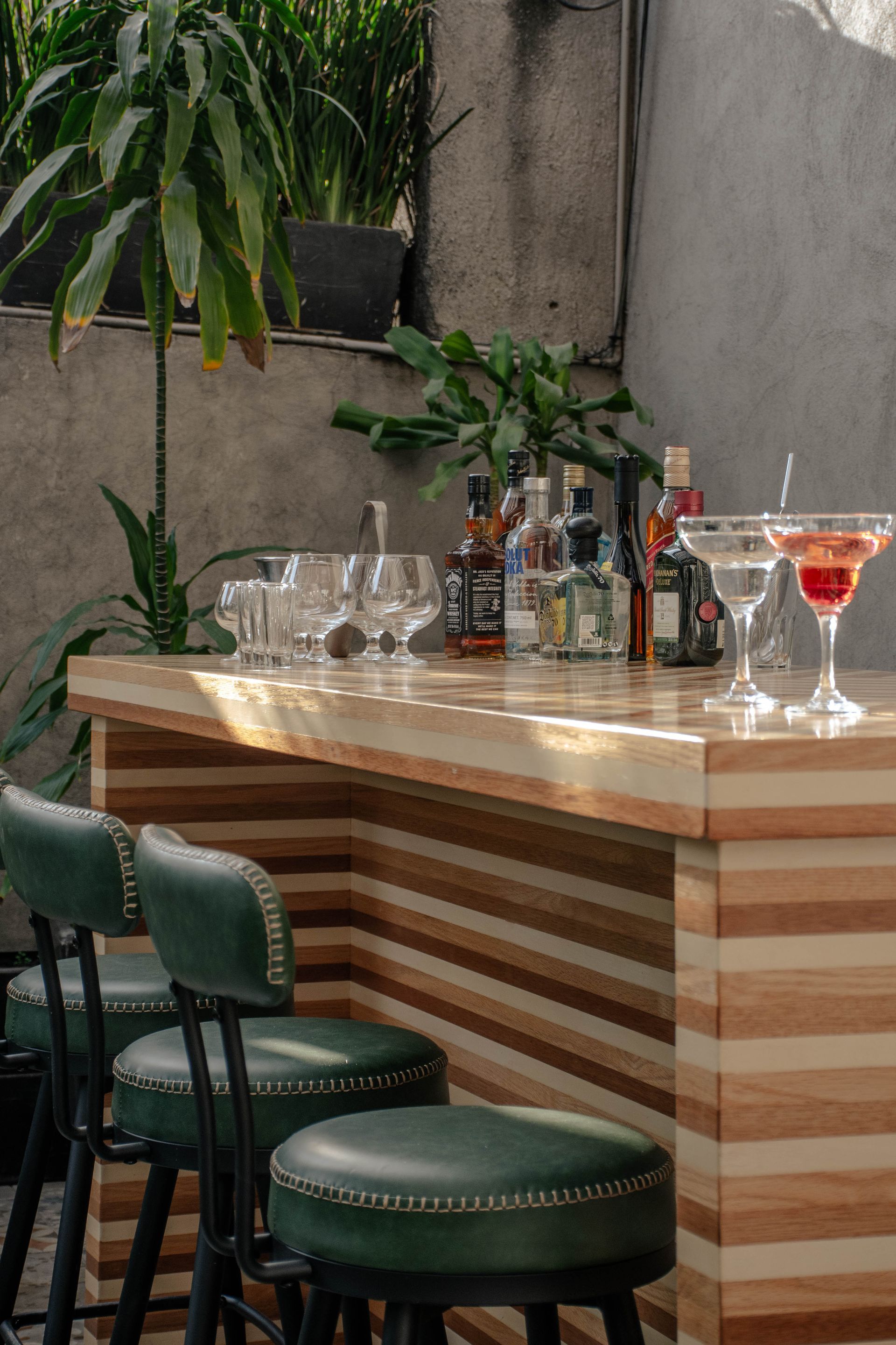 Elegante barra de bar con botellas, vasos y taburetes verdes en un acogedor patio interior