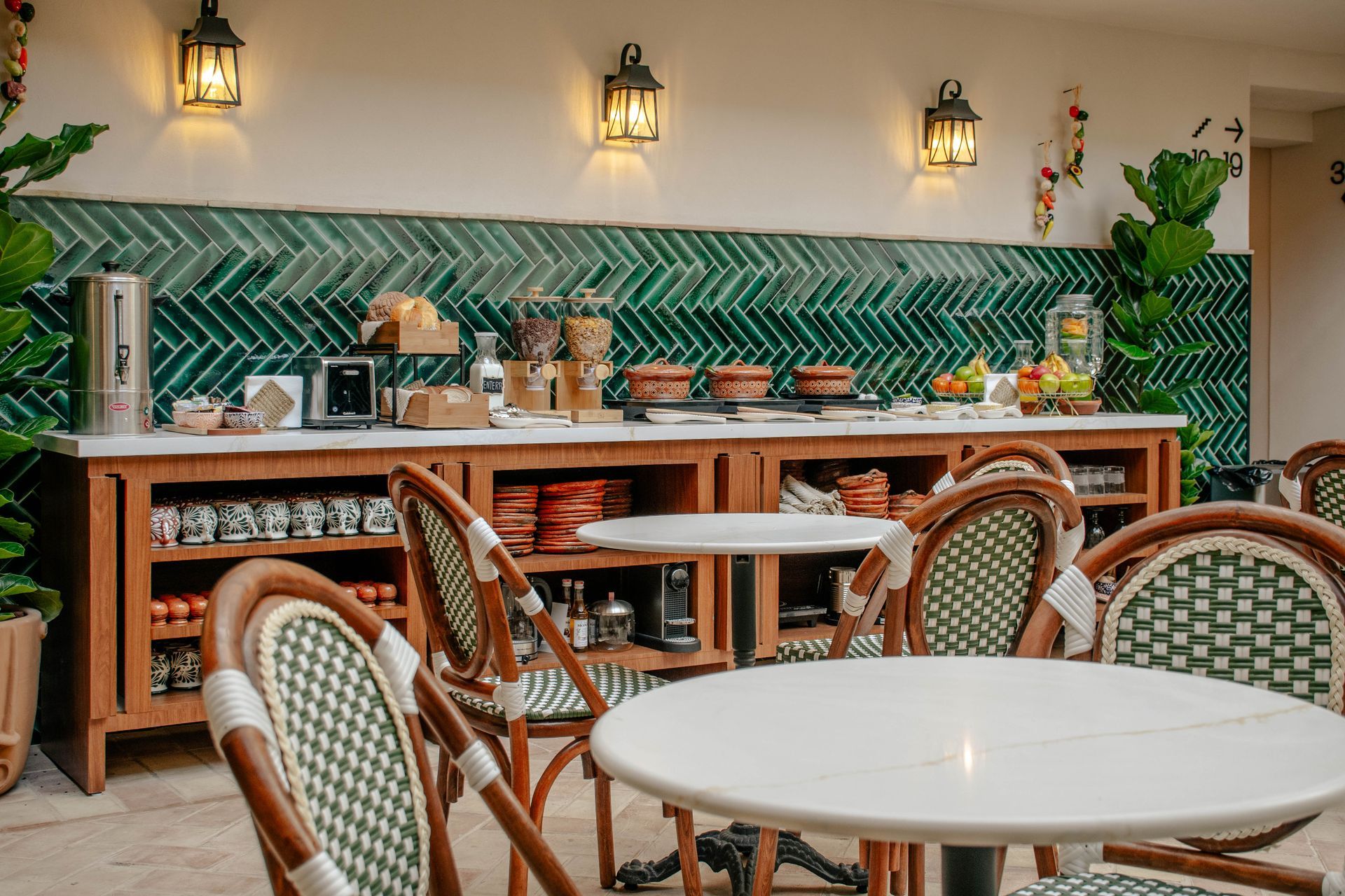 Acogedora terraza de café con sillas de mimbre, mesas redondas blancas y una barra de azulejos verdes en espiga.
