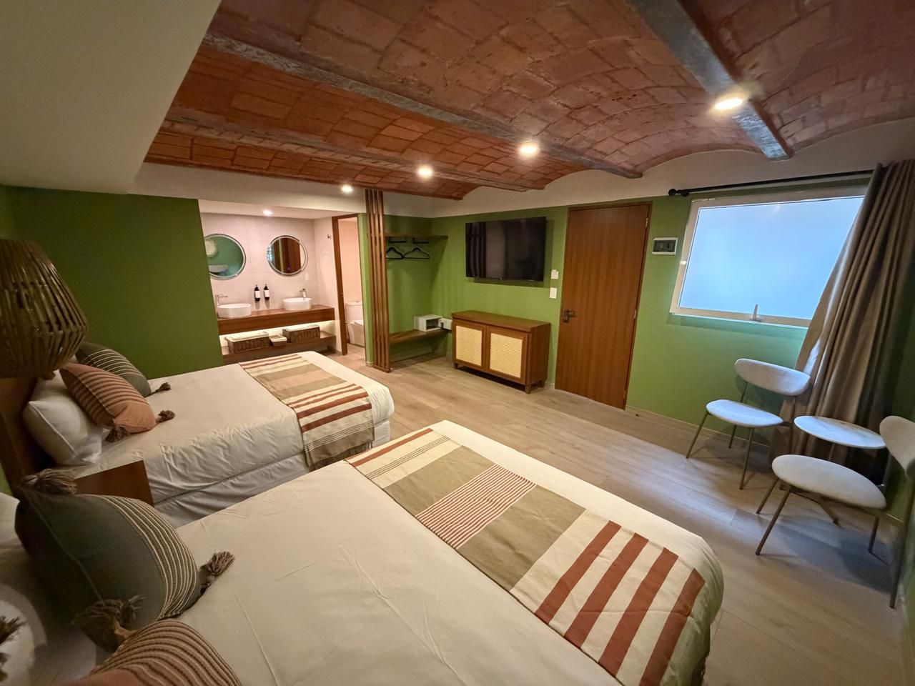 Habitación acogedora con dos camas, paredes verdes, techo de madera y gran ventanal con vistas al mar.