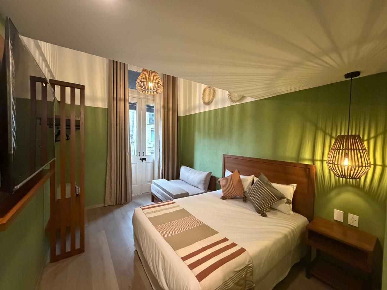 Habitación acogedora con cama, ropa de cama a rayas, paredes verdes, cortinas y luz cálida junto a la cama.