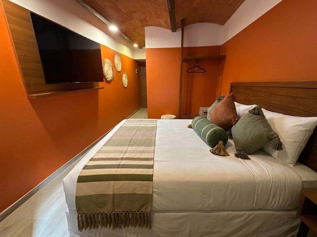 Acogedora habitación de hotel en naranja y blanco con cama, televisor montado en la pared y manta a rayas.
