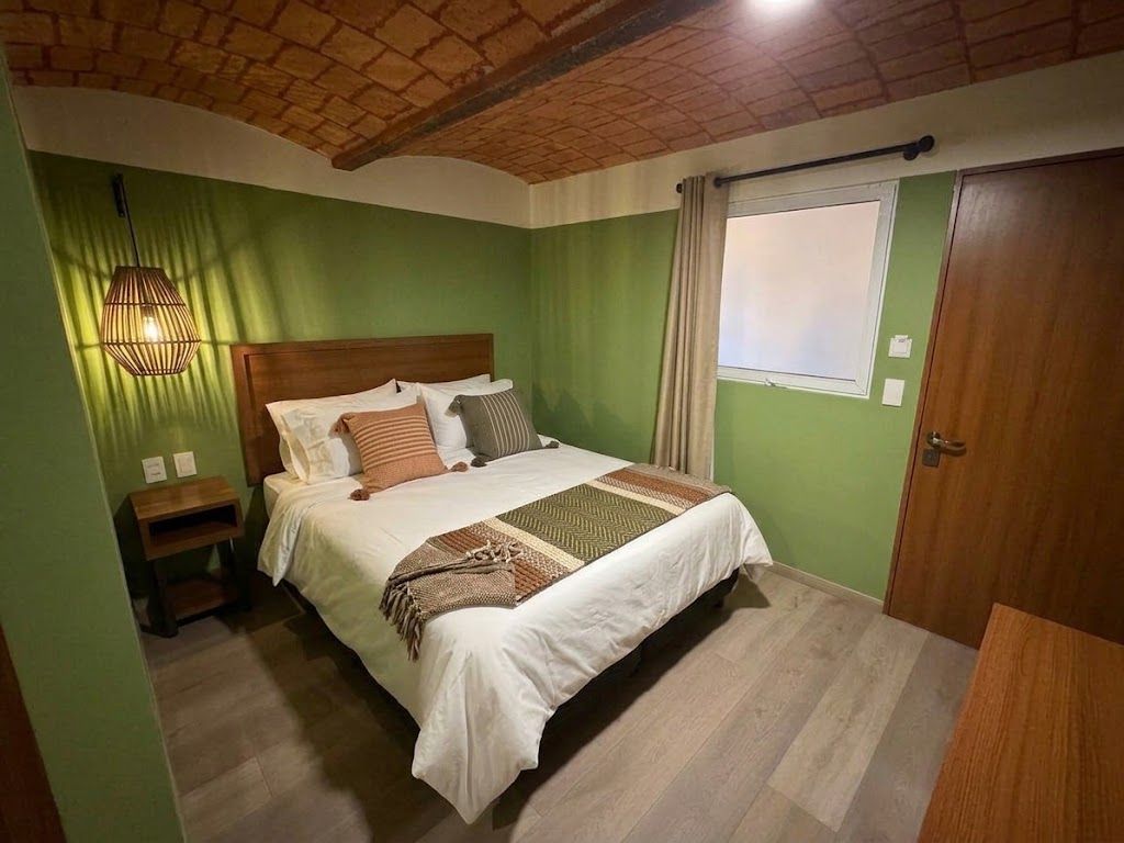 Habitación acogedora con paredes verdes, techo de madera, cama blanca y ventana con cortinas.