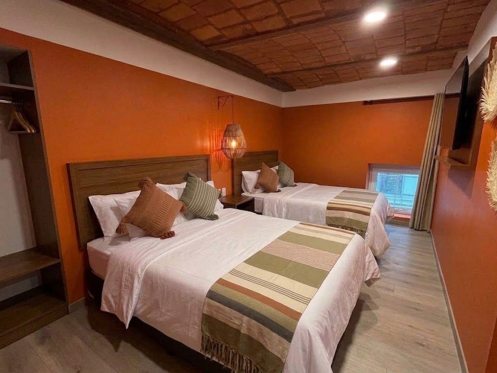 Habitación moderna con dos camas, paredes naranjas, techo de madera y una pequeña ventana.