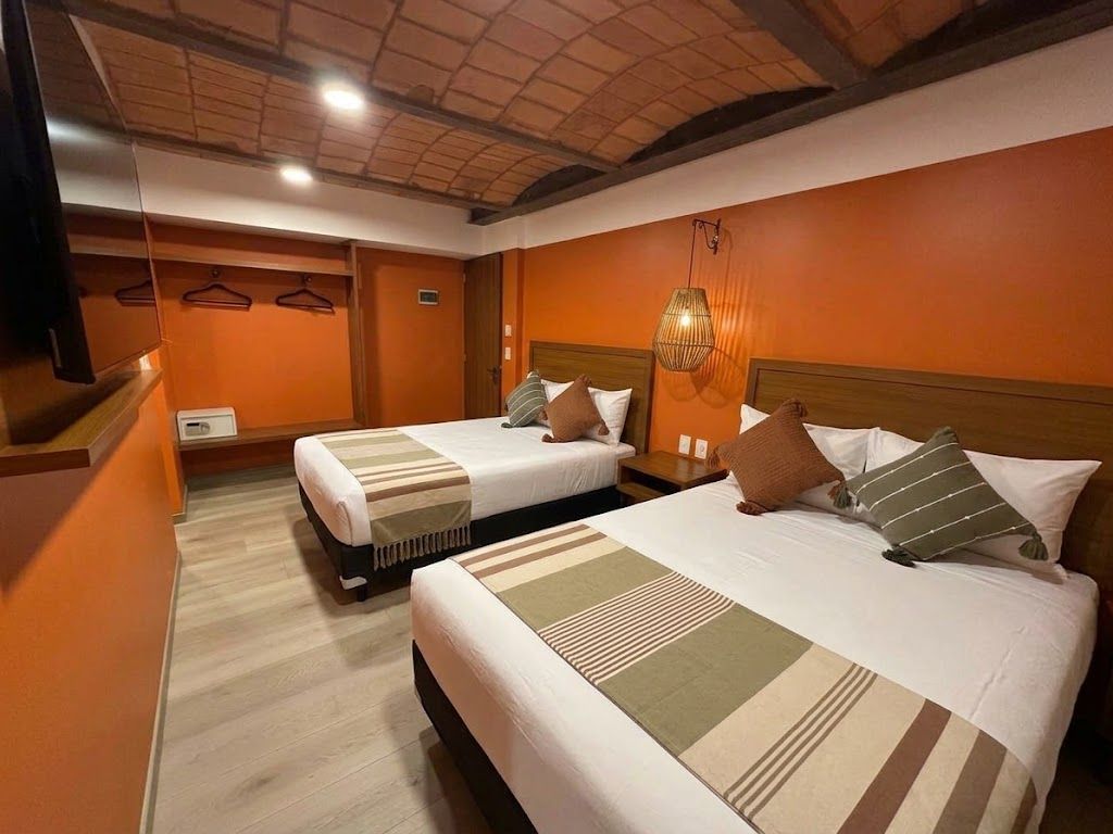 Habitación de hotel naranja con dos camas bien hechas, iluminación cálida y techo de madera.