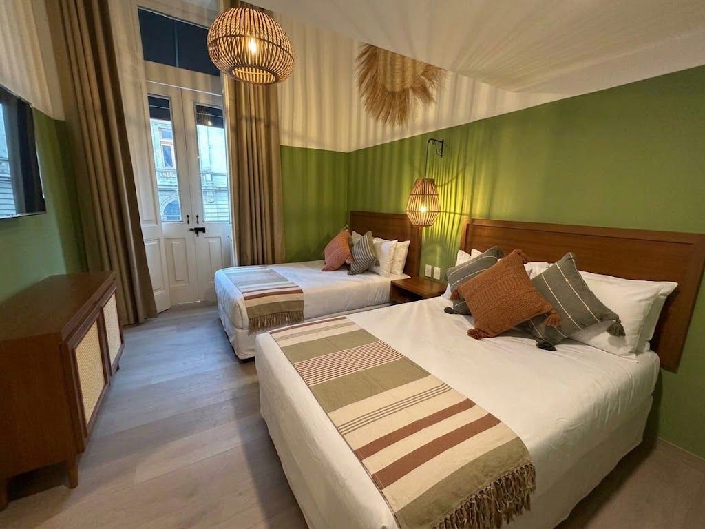 Acogedora habitación de hotel con dos camas individuales, paredes verdes, ropa de cama a rayas y ventana junto a la puerta.
