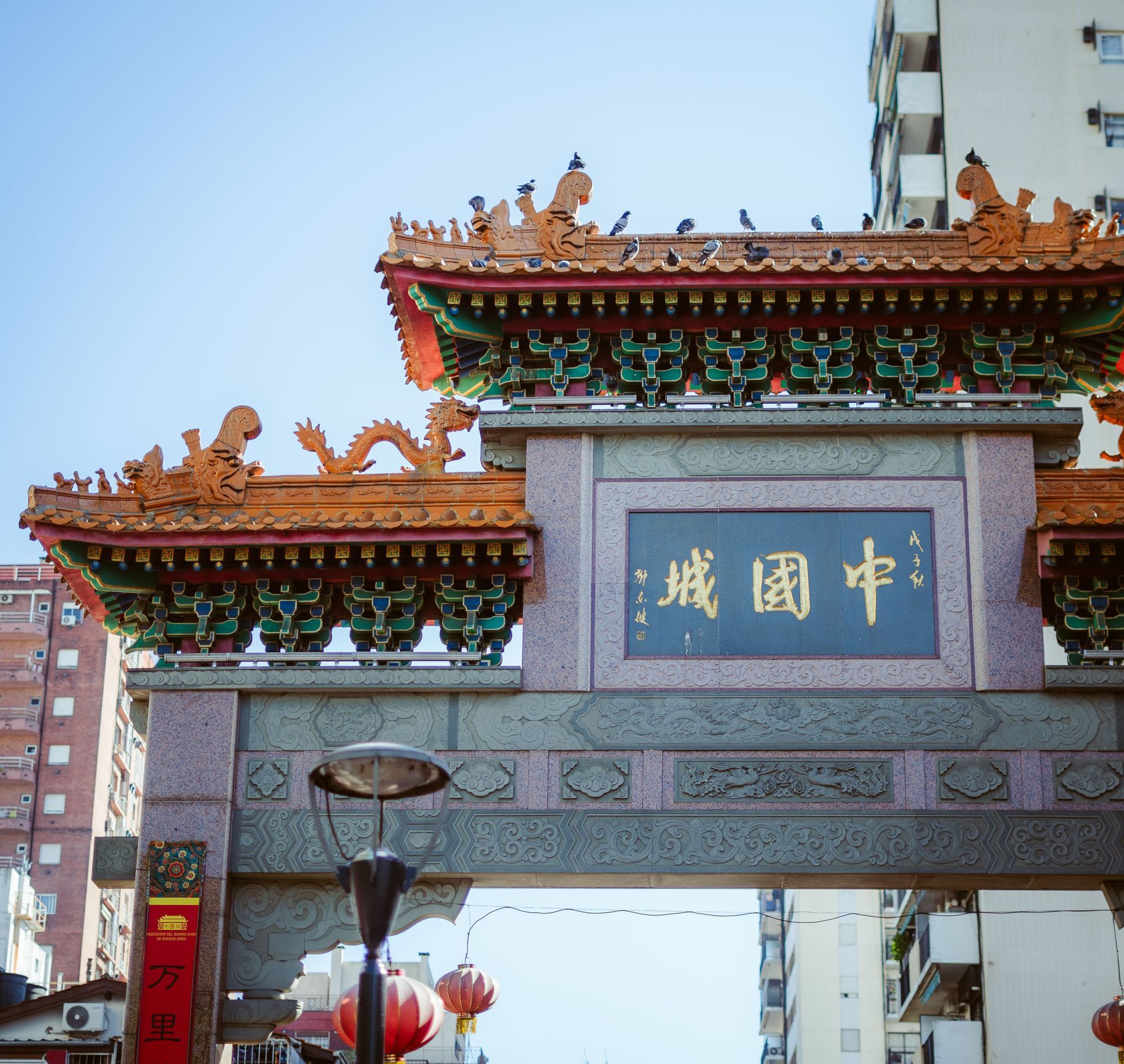 Arco tradicional chino con techo rojo y dorado ornamentado y placa azul en una calle de la ciudad.