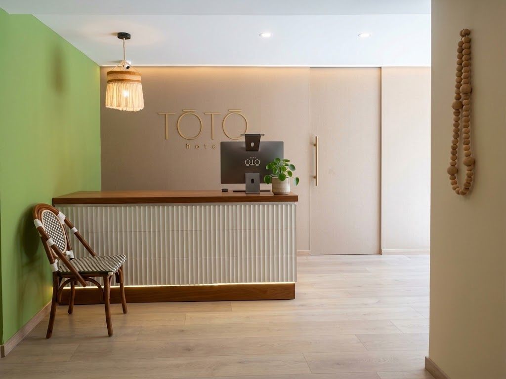 Vestíbulo minimalista con mostrador de recepción de madera, sillas, pared vegetal y lámpara colgante.