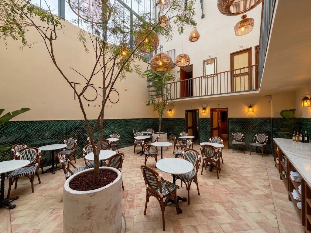 Cafetería con patio, mesas redondas, sillas de mimbre, faroles colgantes y un árbol en el centro.