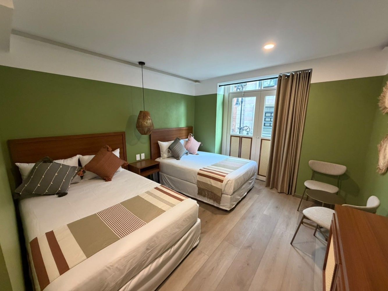 Una habitación de hotel verde con dos camas, una ventana y un pequeño escritorio junto a la pared.