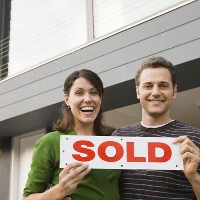 Smiling couple holding a white sign with bold red “SOLD” text outside a house — Murphy Finance Solutions In Zuccoli, NT