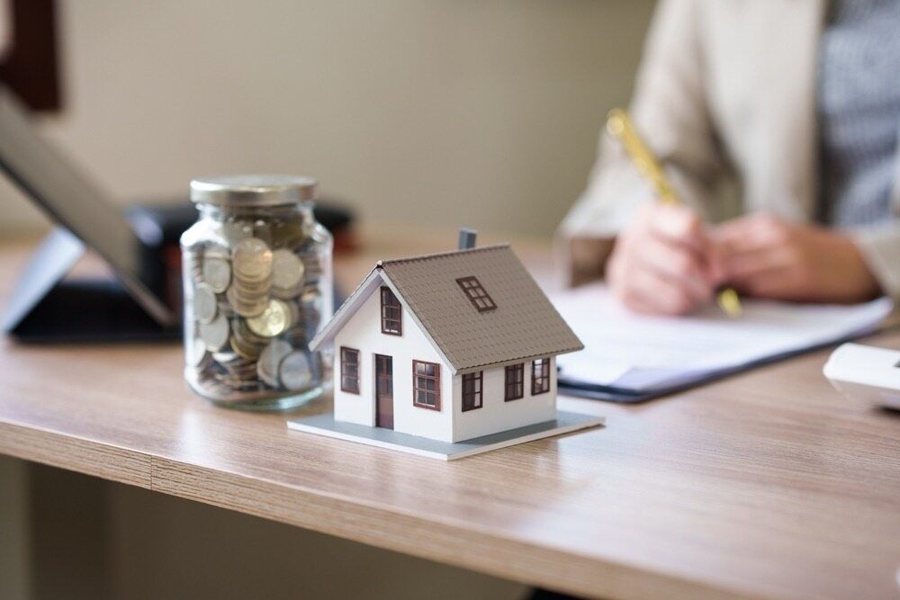 A Model House is Sitting on a Desk Next to a Jar of Coins — Murphy Finance Solutions In Zuccoli, NT