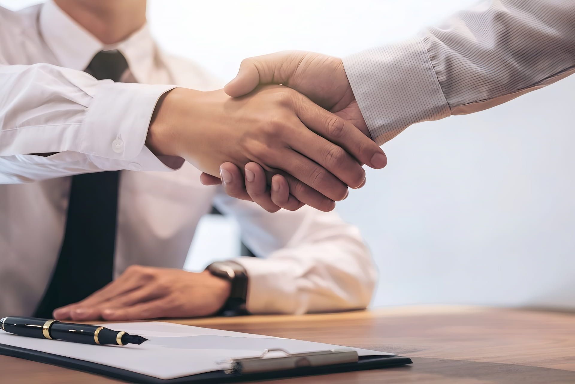 Two professionals shaking hands over a document on a wooden desk — Murphy Finance Solutions In Zuccoli, NT