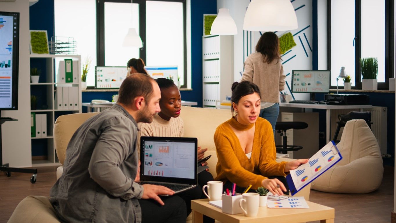 Team collaborating in a modern office around a laptop and chart, with one person presenting a board.