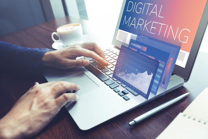 Hands typing on a laptop with a “Digital Marketing” screen on a desk with coffee and a pen