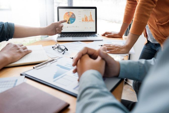 Team meeting around a laptop showing charts and graphs on a conference table