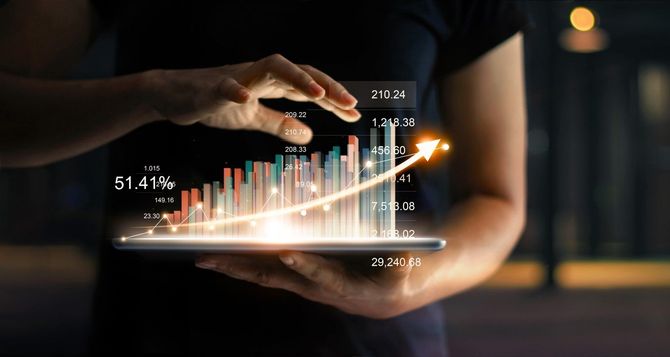 Hands using a tablet displaying glowing financial charts and rising data bars