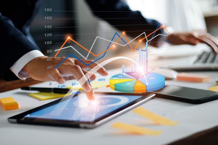 Hands using tablet and phone beside charts and graphs on a desk, showing business analytics.