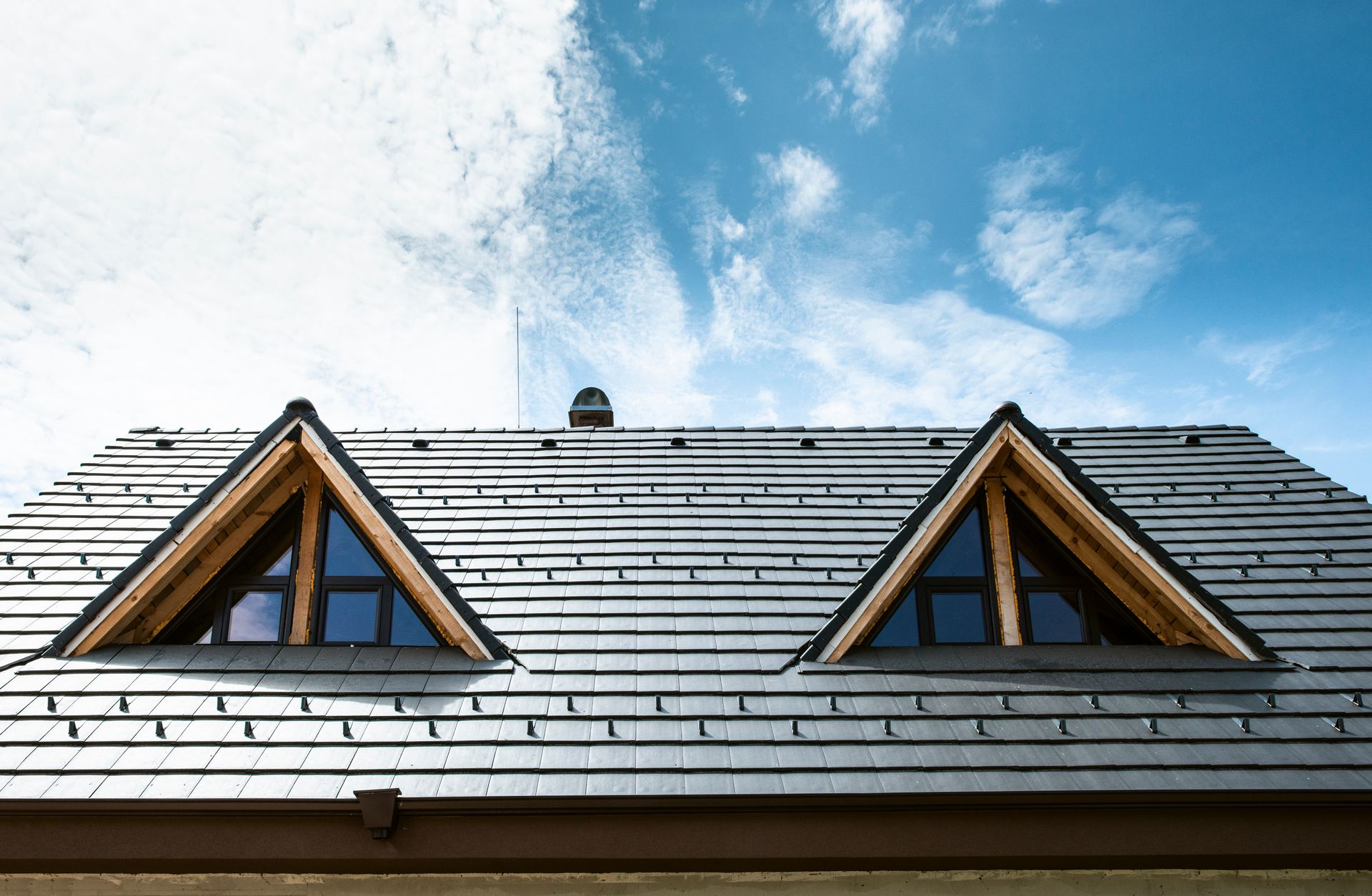 A roof with two triangular dormer windows and a blue sky.