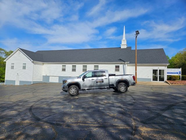 White church with steeple and silver pickup truck in a parking lot under a blue sky.