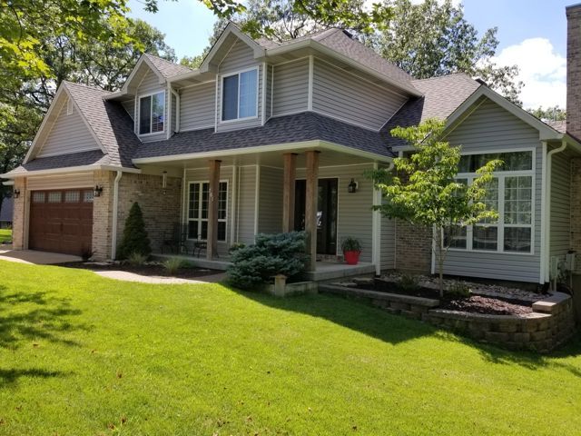 Suburban house with a covered front porch, attached garage, and green lawn on a sunny day