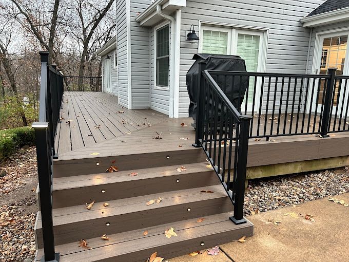 Outdoor wooden deck with steps and black railings beside a gray house