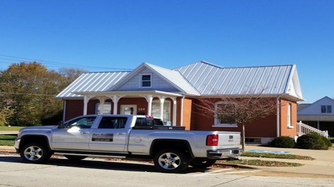Silver pickup truck parked in front of a red brick house with a white porch and metal roof