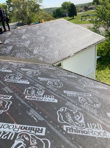 Roofing underlayment on a sloped roof beside a grassy yard and trees