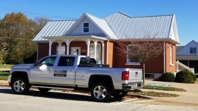 Silver pickup truck parked in front of a brick house with a white porch and metal roof