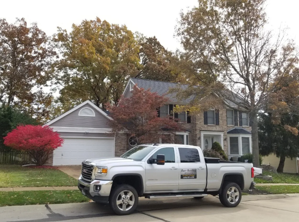Silver pickup truck parked in front of a suburban house with autumn trees and a garage