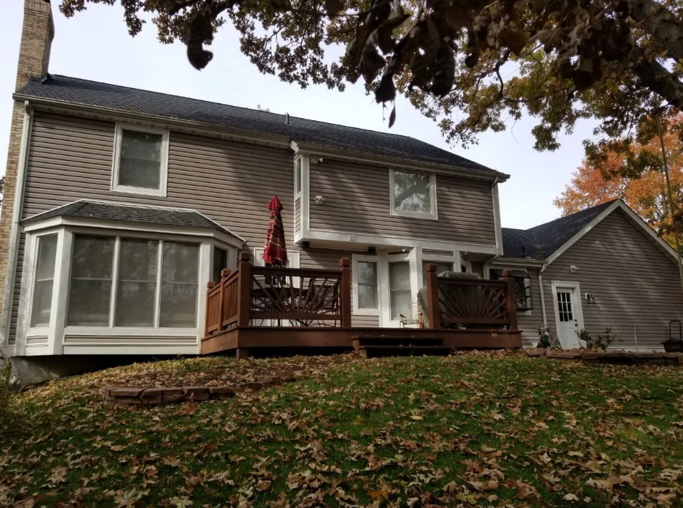 Suburban two-story house with deck, bay window, and autumn leaves on the lawn.