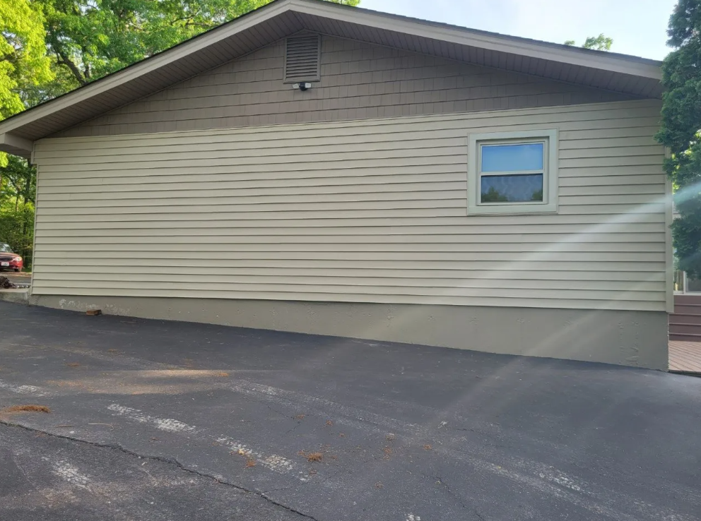 Gray house exterior with a sloped roof and a small window beside a paved driveway