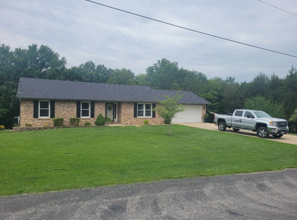 Brick ranch house with black shutters, green lawn, silver truck in driveway.