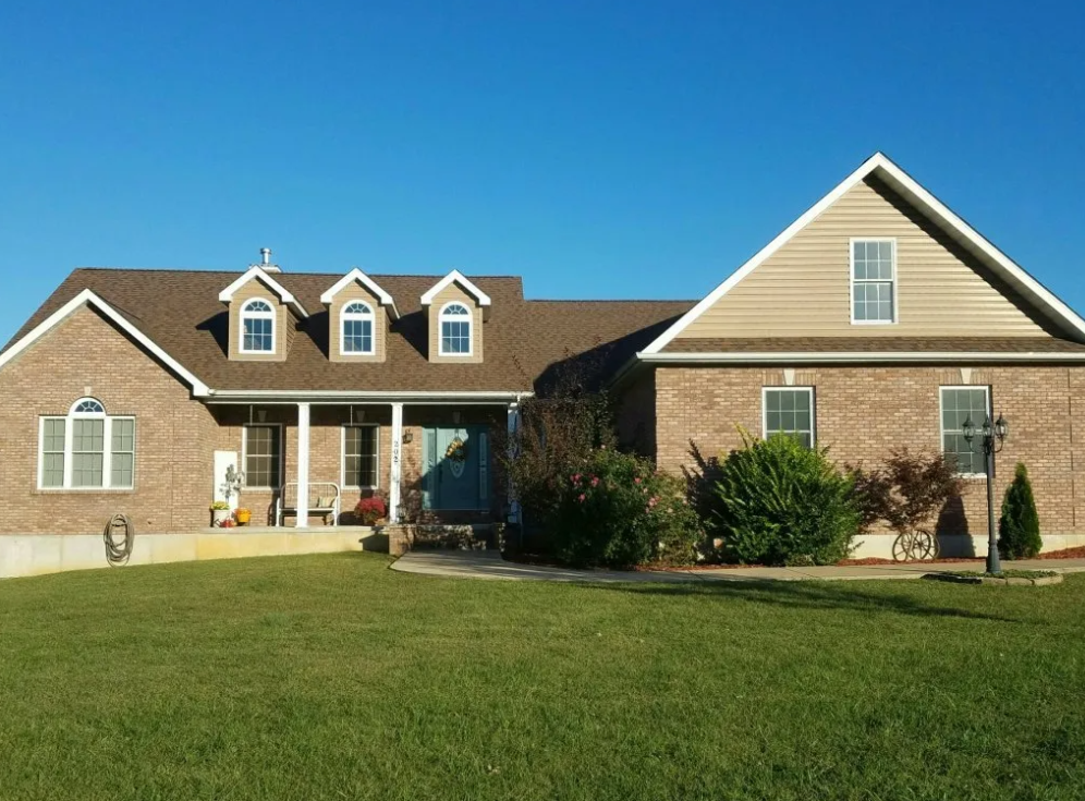 Suburban brick house with white trim, front porch, and green lawn under a clear blue sky