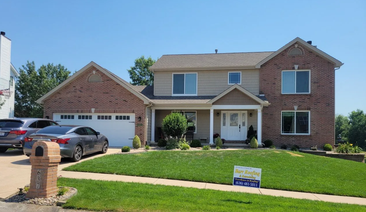 Suburban two-story brick house with garage, driveway, lawn, and parked cars on a sunny day