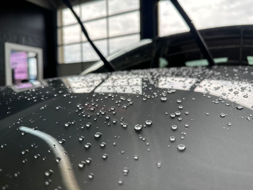 Raindrops on a dark car hood in a garage, with a blurred window and wall in the background