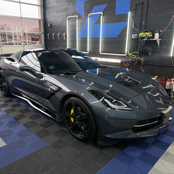 Gray sports car in a detailing garage with blue floor mats and neon wall lights