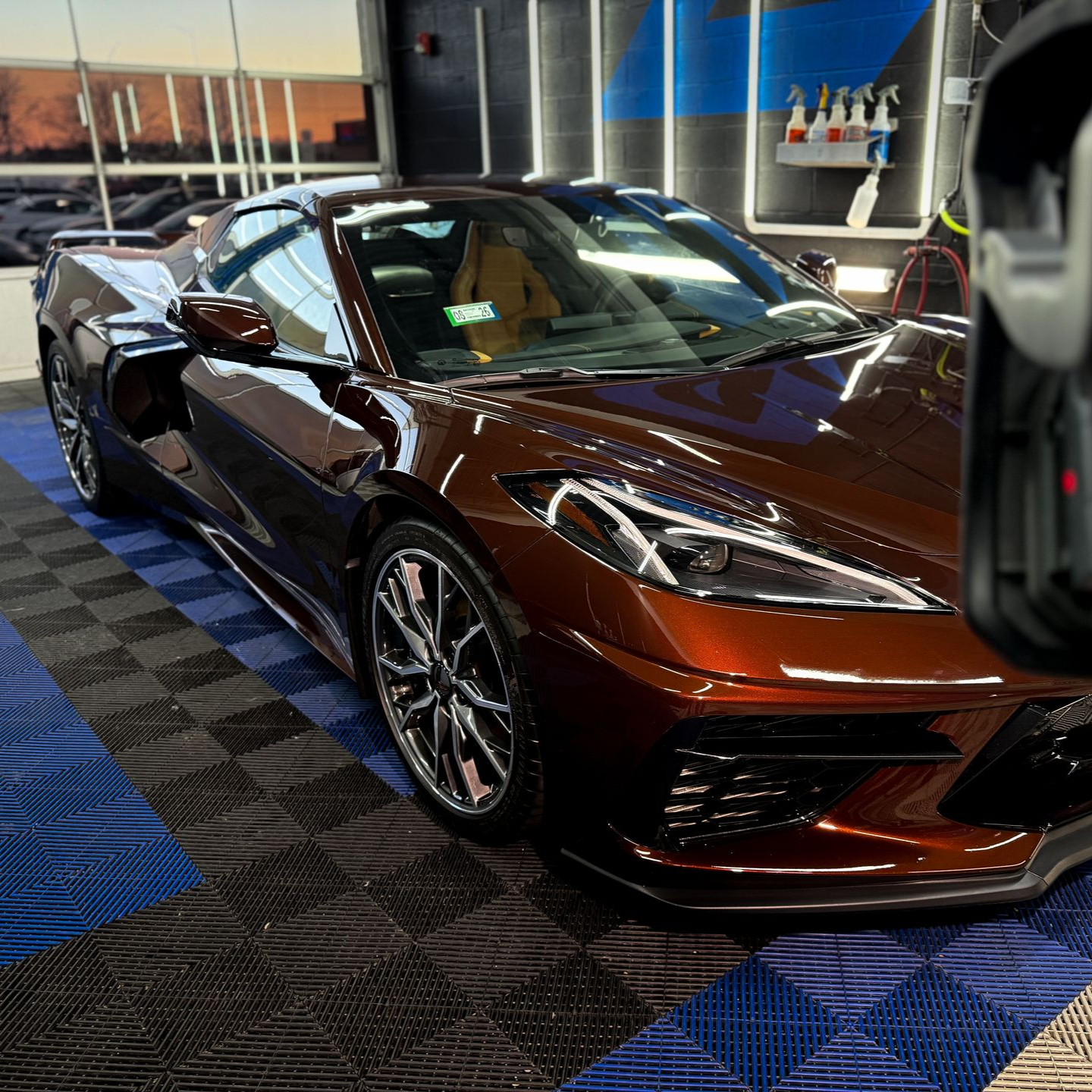 Metallic brown sports car displayed indoors on a patterned showroom floor.