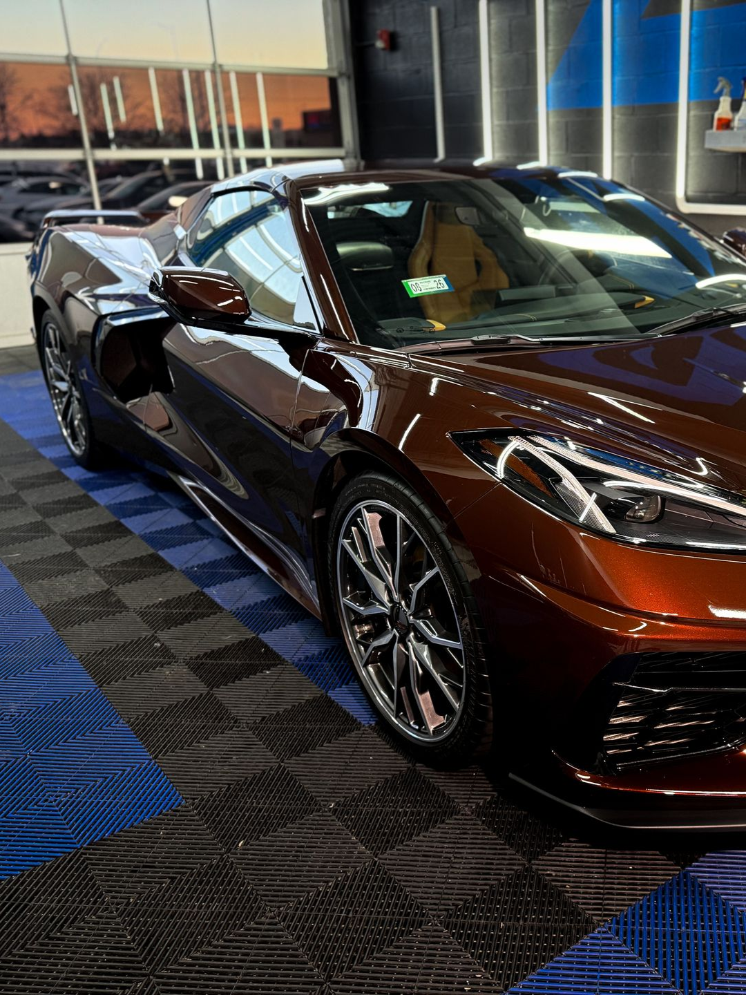 Dark brown sports car on display in a showroom with blue and black flooring.