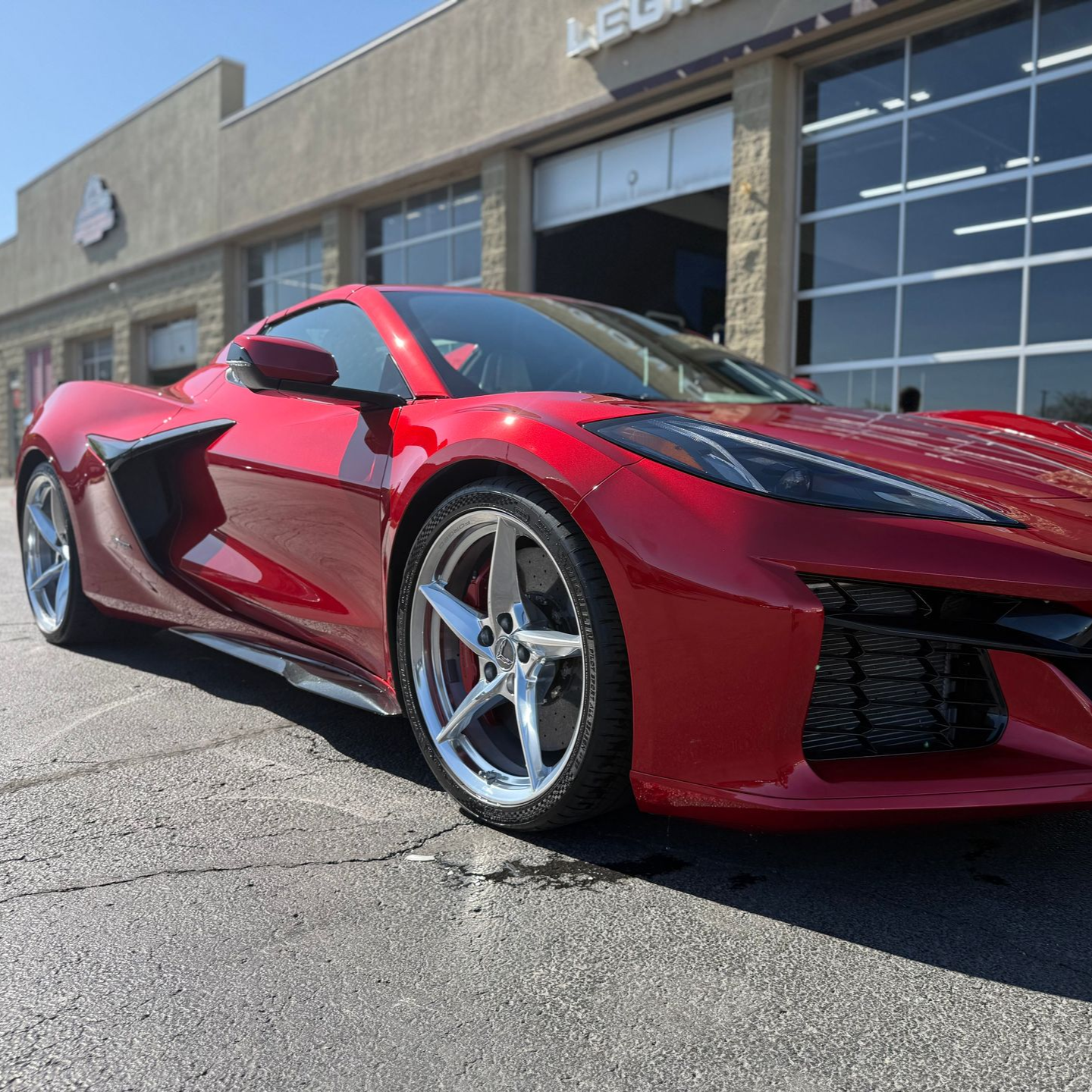 Red sports car parked outside a dealership, shown from the front-left side.
