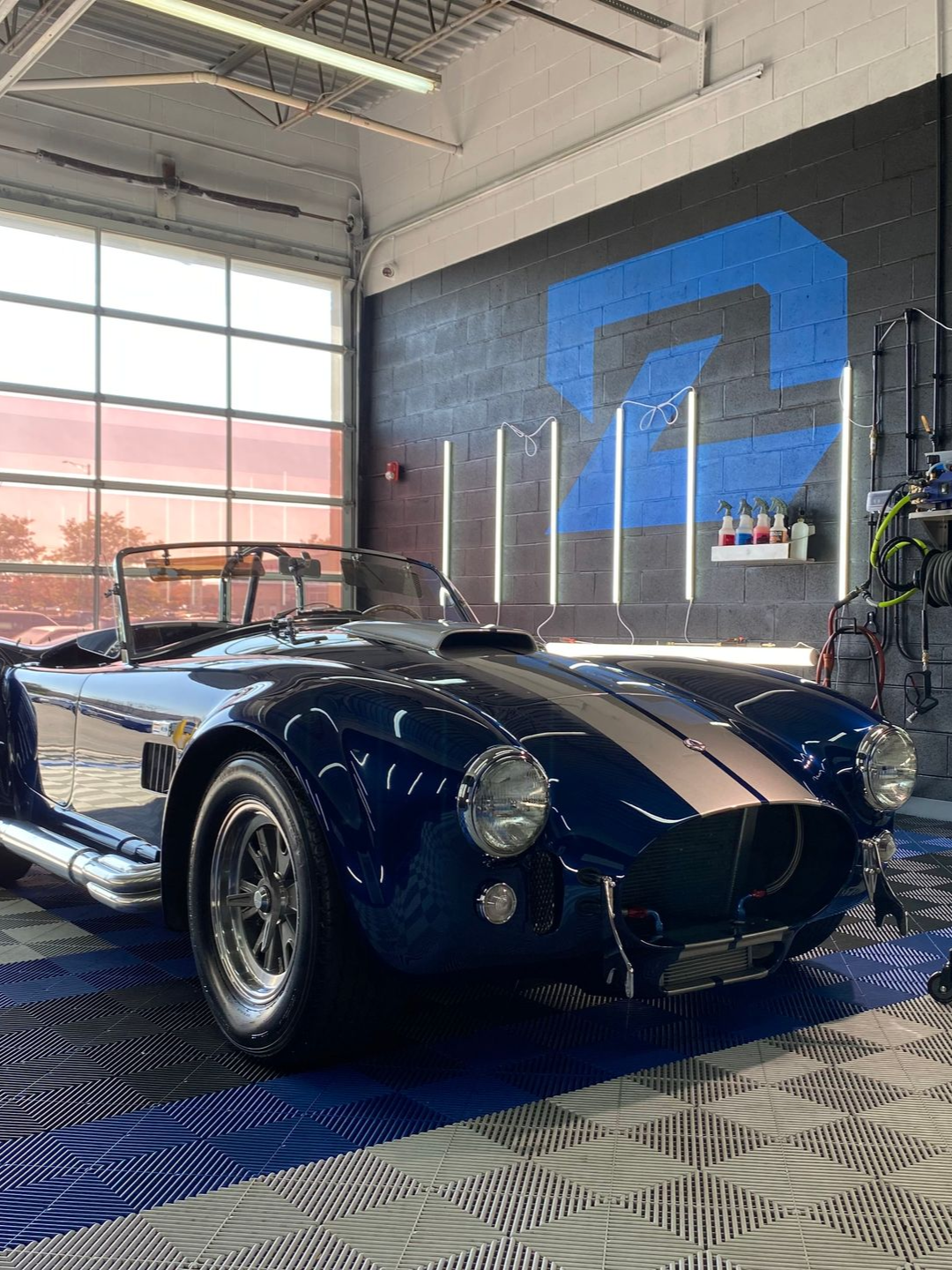 Classic dark blue convertible sports car in a garage with a blue wall mural and large windows